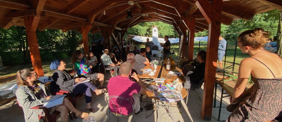 Outside at the CPU. A large group at a workshop. All are under a wooden structure with a roof and open sides.